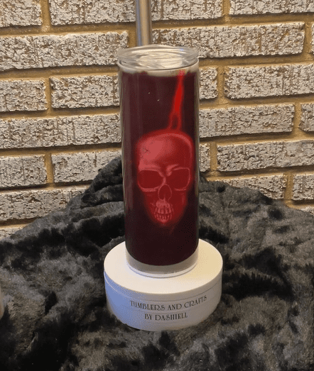 A candle with a skull on it sitting in front of a brick wall.