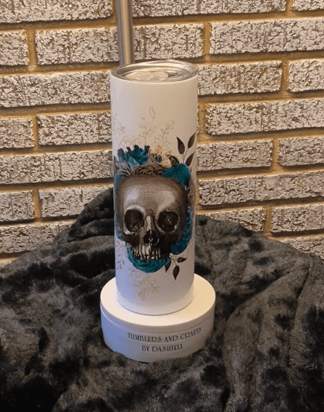 A candle with a skull on it sitting in front of a brick wall.