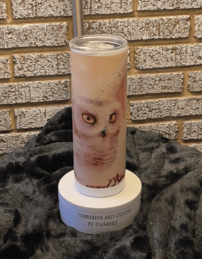 A candle with an owl on it sitting in front of a brick wall.