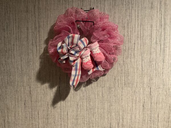 A pink wreath with plaid bow hanging on the wall.